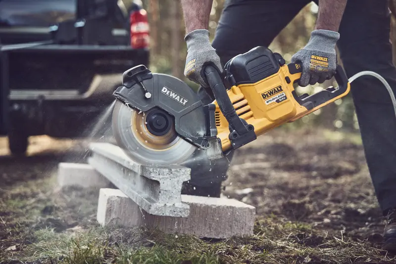 DEWALT power saw cutting concrete outdoors, operator wearing gloves for safety.